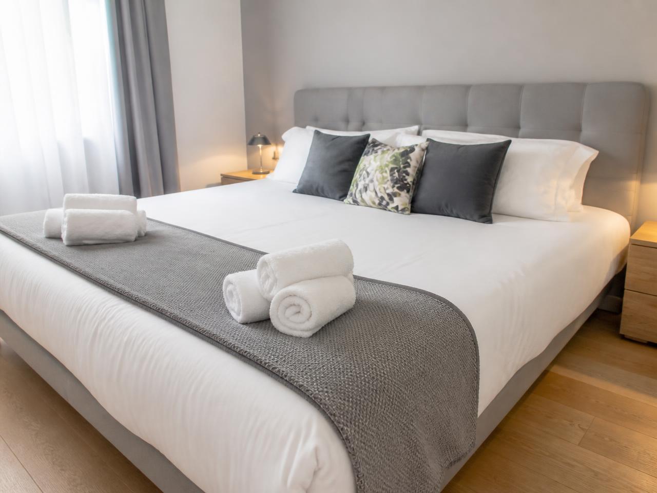 Habitación de apartamento turístico con cama montada, ropa de cama blanca y toallas enrolladas tras la limpieza